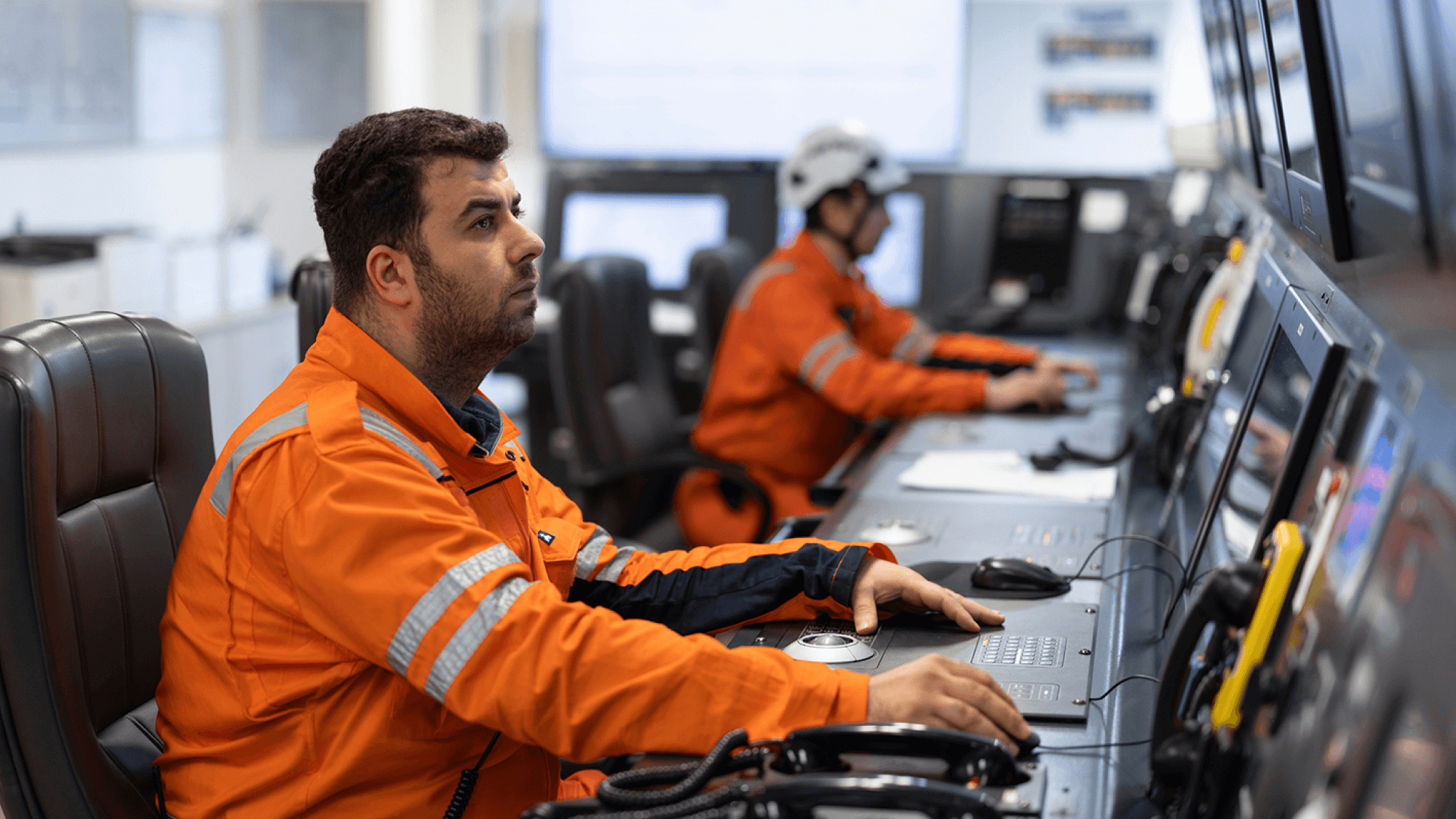 "Offshore operations personnel monitoring vessel performance and operational data from a maritime control room equipped with multiple digital monitoring systems."
