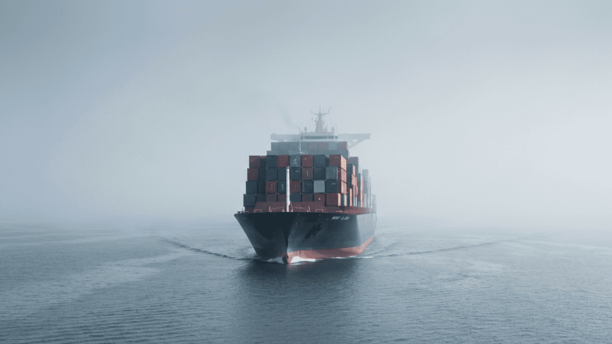 "Container ship sailing through foggy ocean carrying stacked cargo containers in low-visibility conditions"